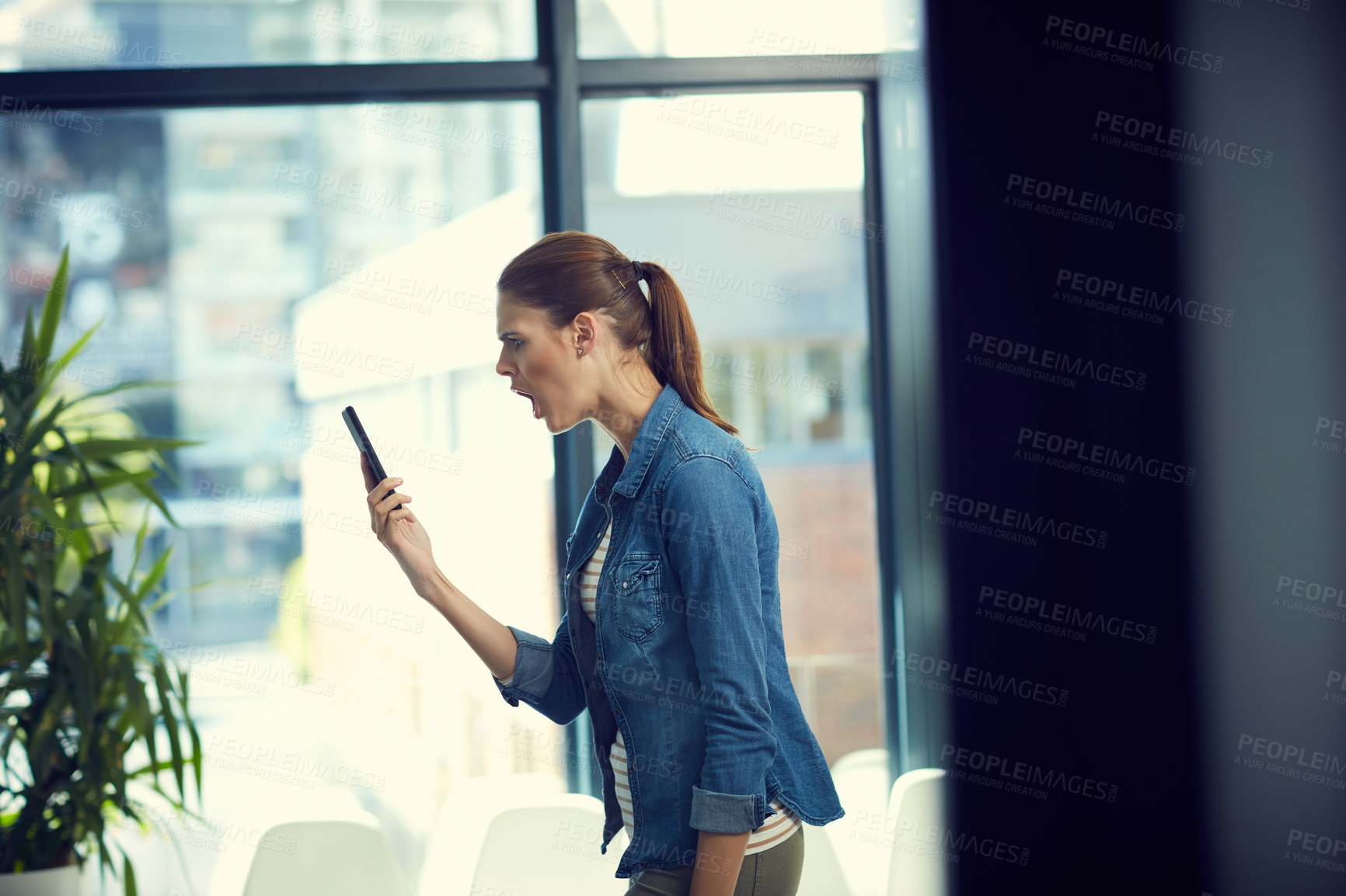 Buy stock photo Shot of a young businesswoman using a mobile phone and looking angry in a modern office