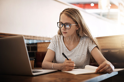 Buy stock photo Cropped shot of a focussed young student using her laptop to study at a table in a cafe