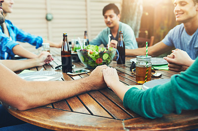Buy stock photo Shot of a group of young friends holding hands together around a table outside in a garden