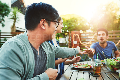 Buy stock photo Shot of two young man passing a pizza slice to each other around a table in an outside gathering with friends