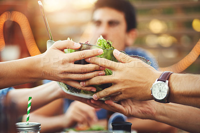 Buy stock photo Shot of two unrecognizable friends passing each other a salad bowl around a table amongst friends in an outdoor gathering