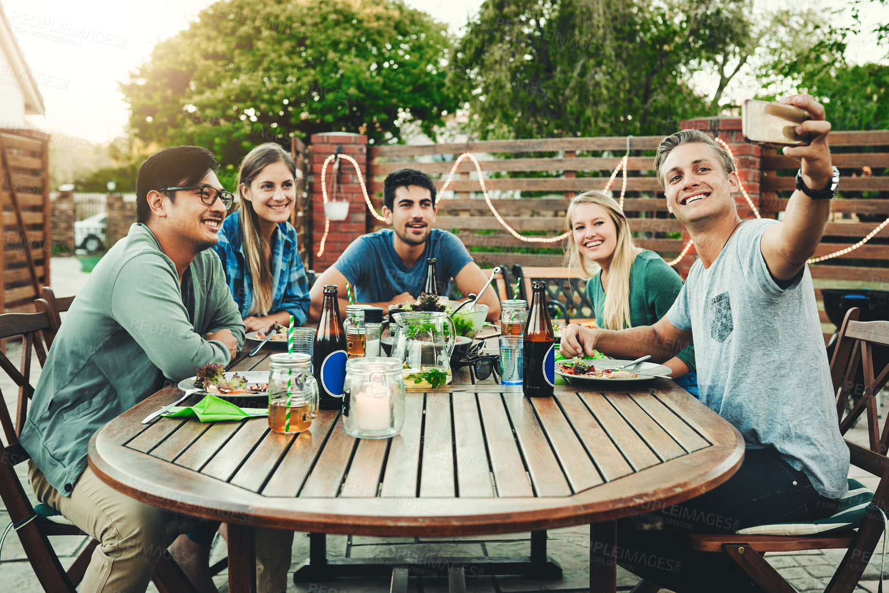 Buy stock photo Shot of a group of young friends posing together around a table while taking a selfie outdoors