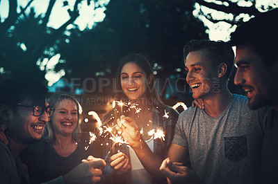 Buy stock photo Shot of a group of cheerful young friends having fun with sparklers together outside in the evening