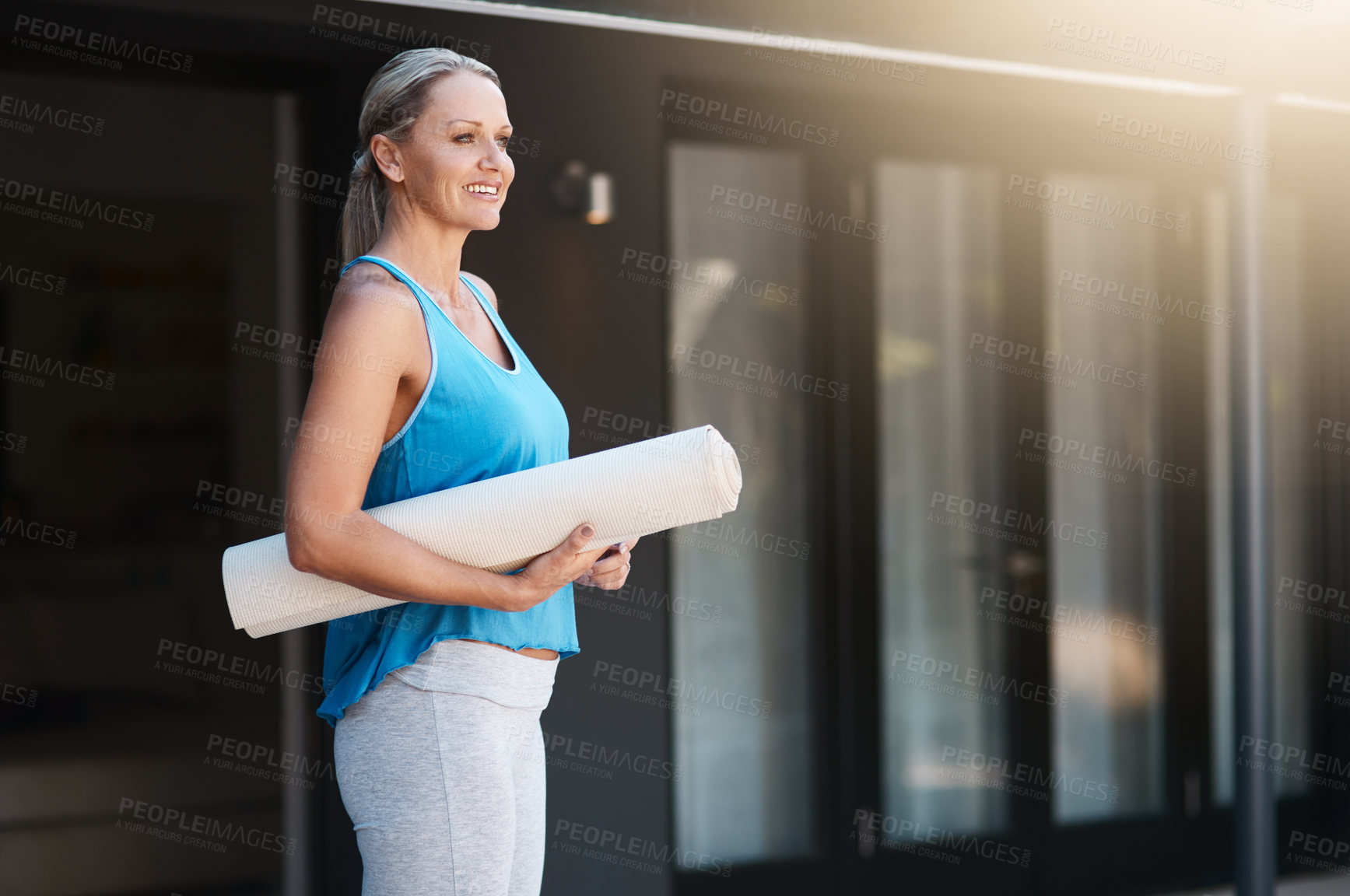 Buy stock photo Shot of a mature woman smiling and holding her yoga mat outside of her home in the morning
