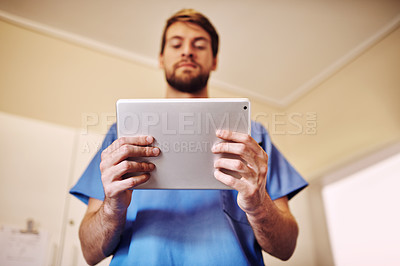 Buy stock photo Shot of a young doctor using his digital tablet in his office