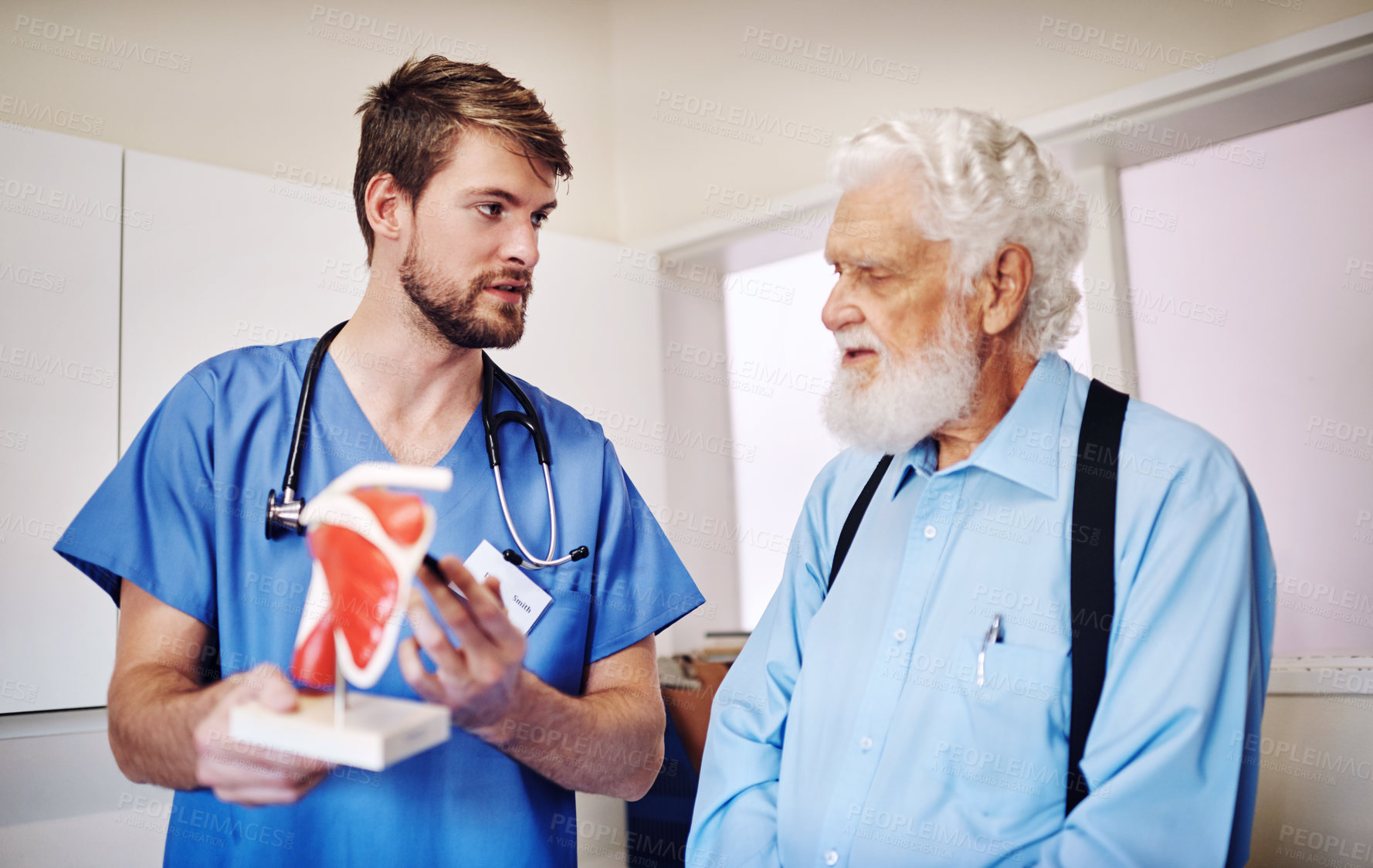 Buy stock photo Shot of a young doctor using a model to explain a diagnosis to his senior patient