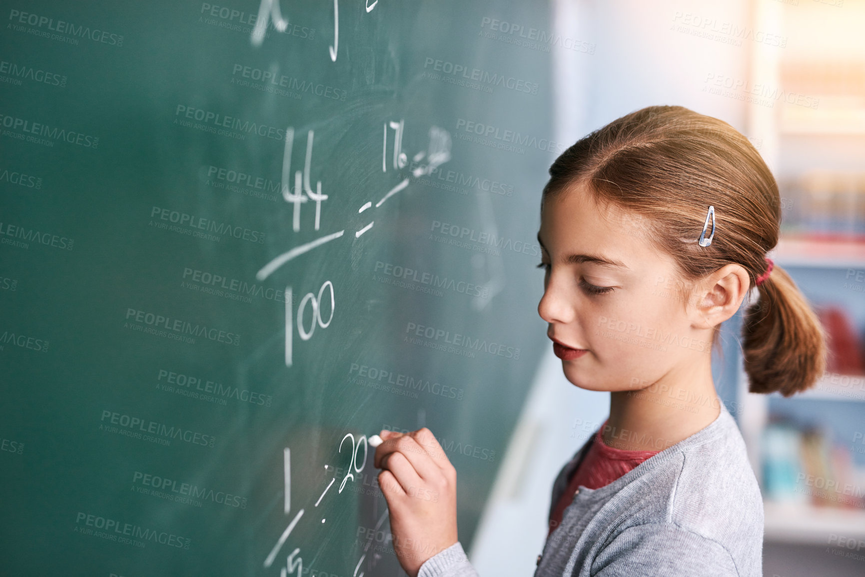 Buy stock photo Cropped shot of a focussed young elementary school kid writing answers to math questions on a green chalkboard in the classroom