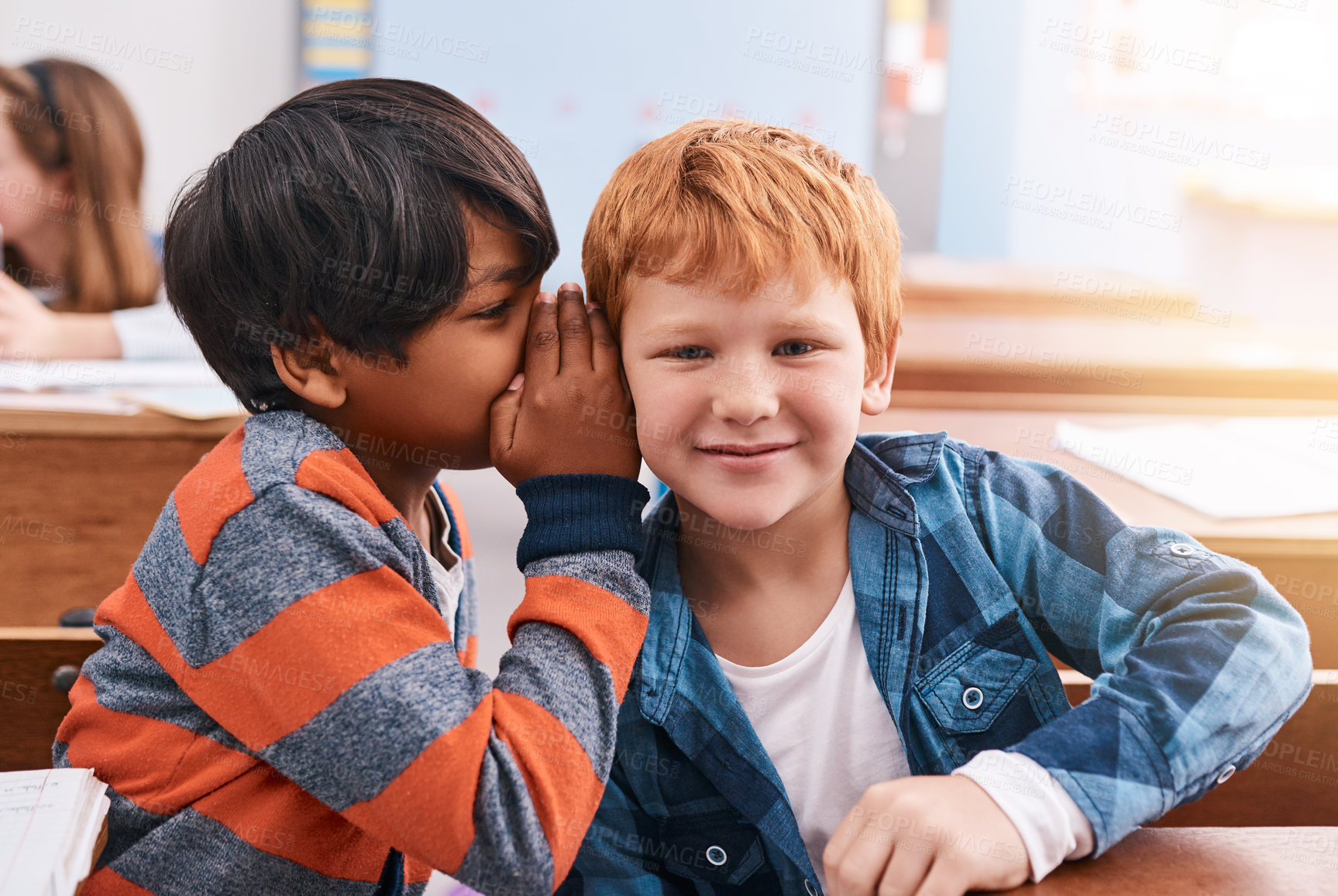 Buy stock photo Cropped shot of elementary school kid whispering into another student's ear inside of the classroom