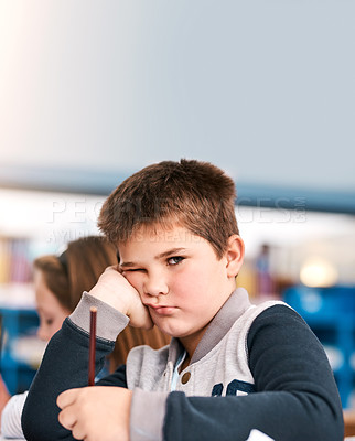 Buy stock photo Portrait of shot of a grumpy elementary school kid sitting in class trying to do school work