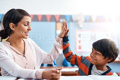 Buy stock photo Shot of a cheerful young female teacher giving her student a high five for doing a great job in the classroom