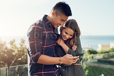 Buy stock photo Shot of an affectionate young couple using a cellphone together while relaxing outdoors