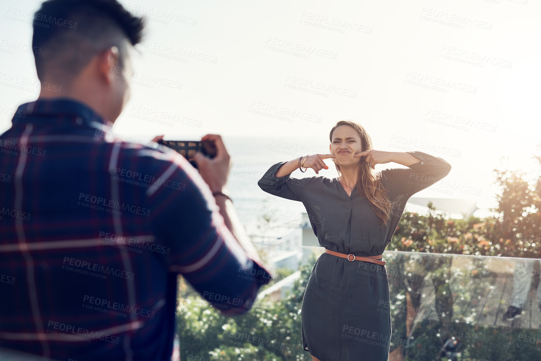 Buy stock photo Shot of an attractive young woman making funny faces while her boyfriend takes pictures of her outdoors