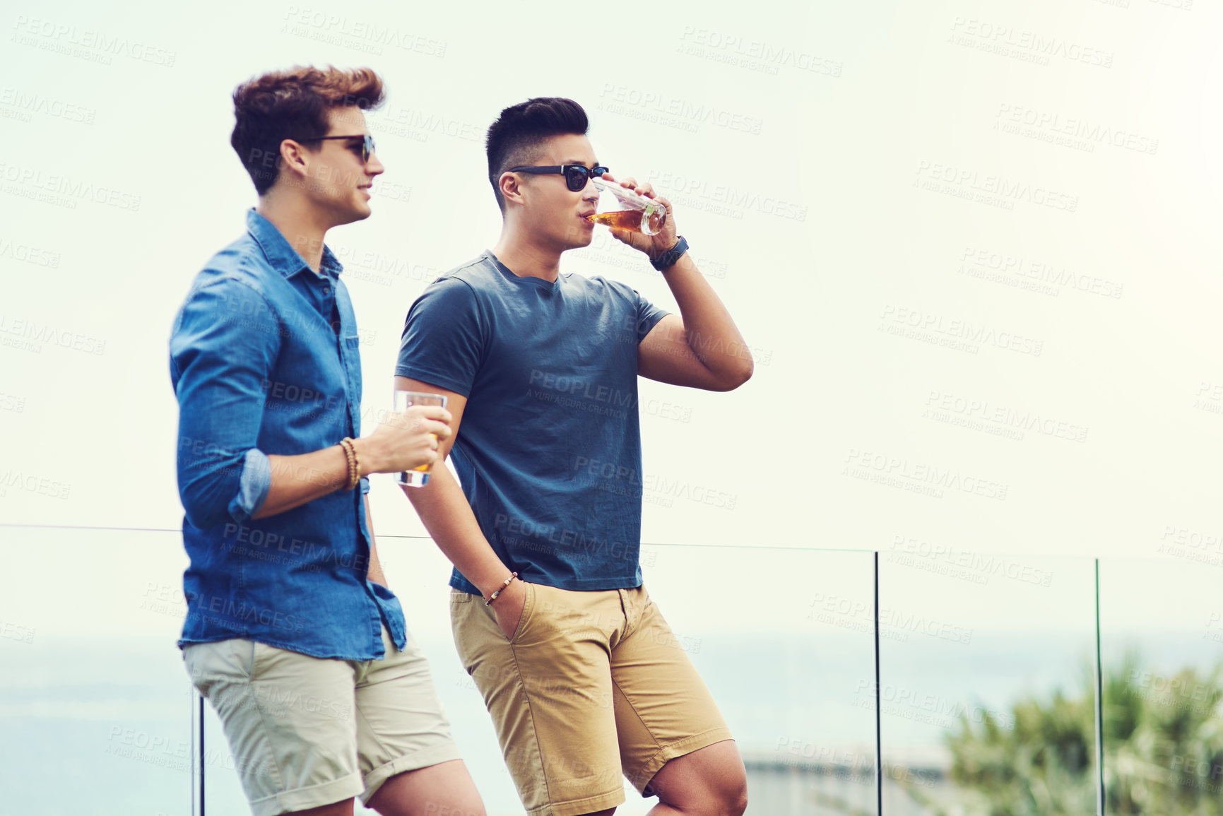 Buy stock photo Shot of two handsome young men having drinks and relaxing outdoors while on holiday