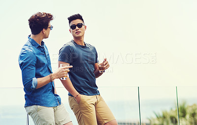 Buy stock photo Shot of two handsome young men having drinks and relaxing outdoors while on holiday