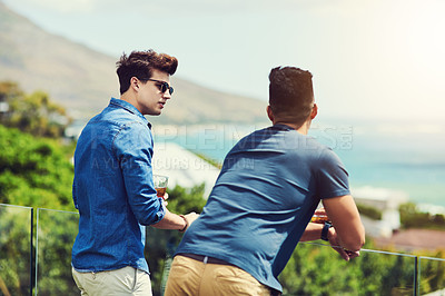 Buy stock photo Rearview shot of two handsome young men having drinks and relaxing outdoors while on holiday