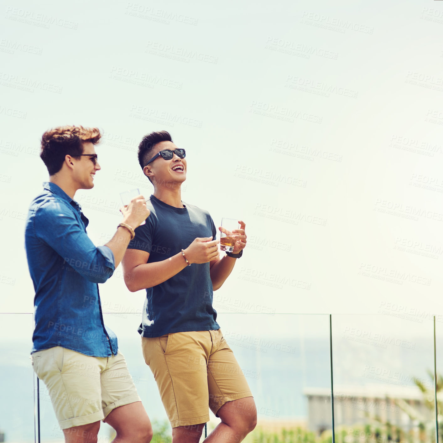 Buy stock photo Shot of two handsome young men having drinks and relaxing outdoors while on holiday