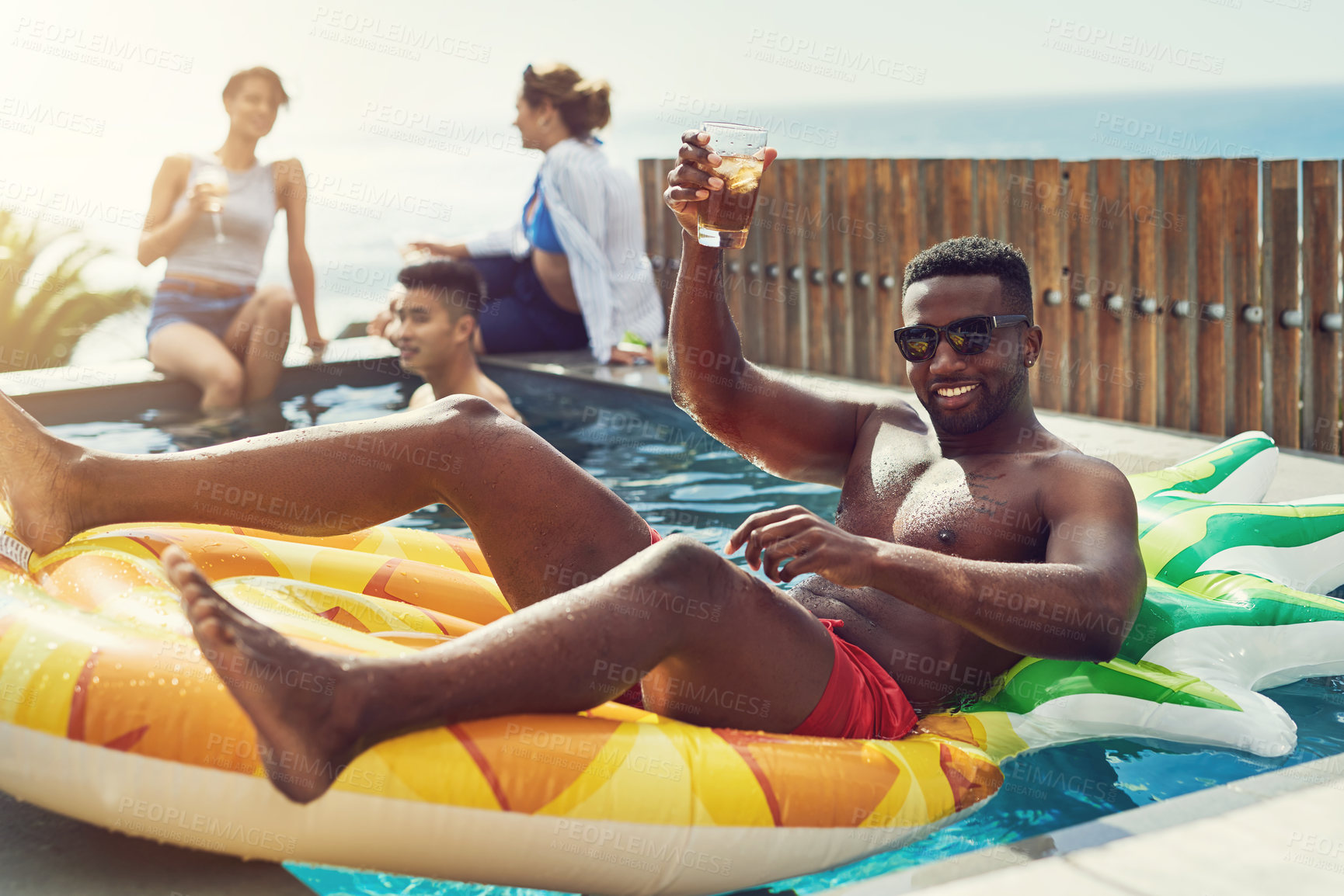 Buy stock photo Portrait of handsome young man raising up his glass for a toast while relaxing in a pool outdoors with friends