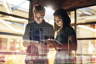 Buy stock photo Shot of two young businesspeople using their digital tablets in their office at work