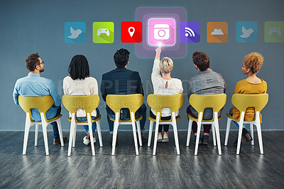 Buy stock photo Rearview shot of a group of businesspeople sitting on chairs and picking icons against a blue background