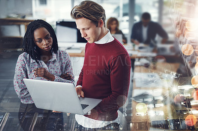 Buy stock photo Shot of two young businesspeople using a laptop together with their colleagues working in the background at work