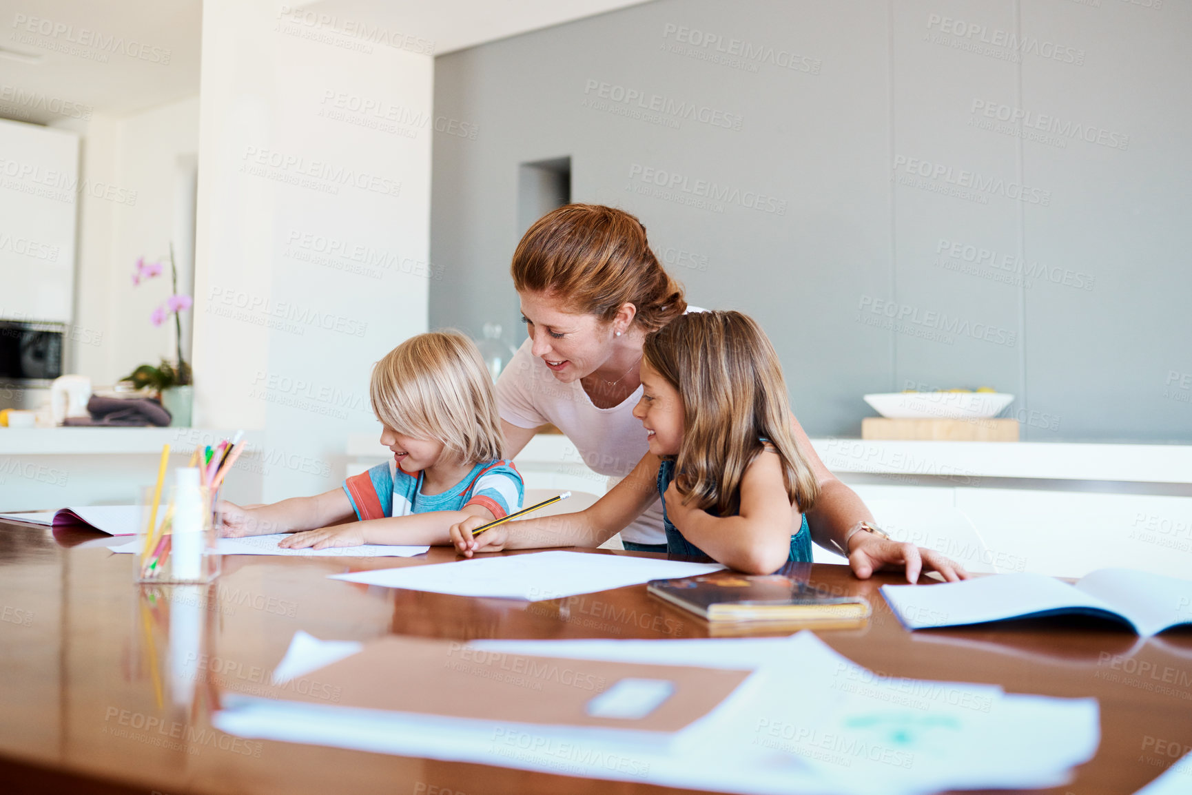 Buy stock photo Shot of a young mother helping her two small children with their homework at home