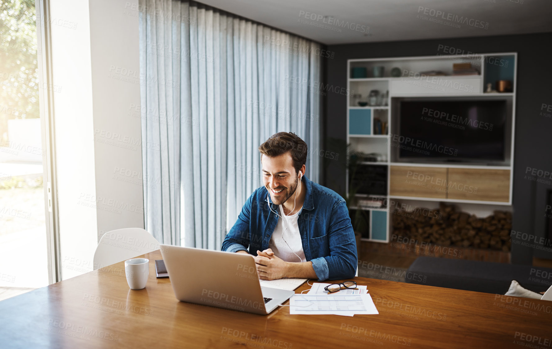 Buy stock photo Shot of a handsome young businessman sitting down and watching online videos on his laptop while working from home