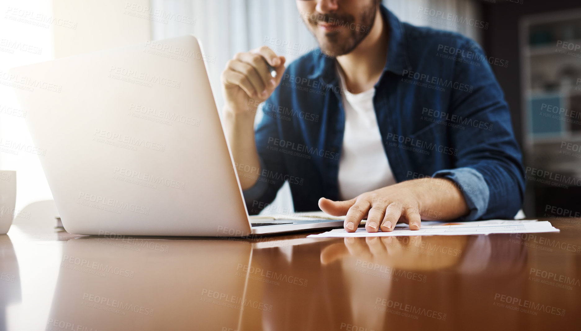 Buy stock photo Shot of a handsome young businessman sitting down and using his laptop while working from home