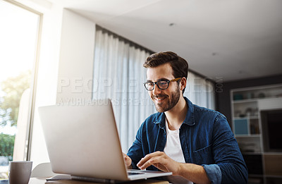 Buy stock photo Shot of a handsome young businessman sitting down and using his laptop while working from home