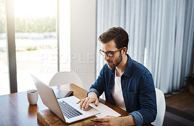 Buy stock photo Shot of a handsome young businessman sitting down and using his laptop to do some online shopping while working from home