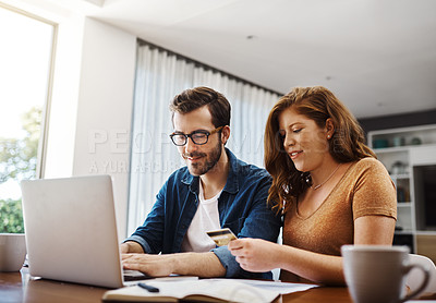 Buy stock photo Shot of a young couple doing some online shopping on a laptop together over the weekend at home