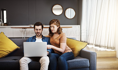 Buy stock photo Shot of a young couple seated on a couch and doing some financial planning together on a laptop at home