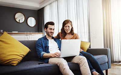 Buy stock photo Shot of a young couple seated on a couch and doing some financial planning together on a laptop at home