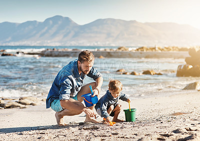 Buy stock photo Shot of a father and his little son building sandcastles together at the beach