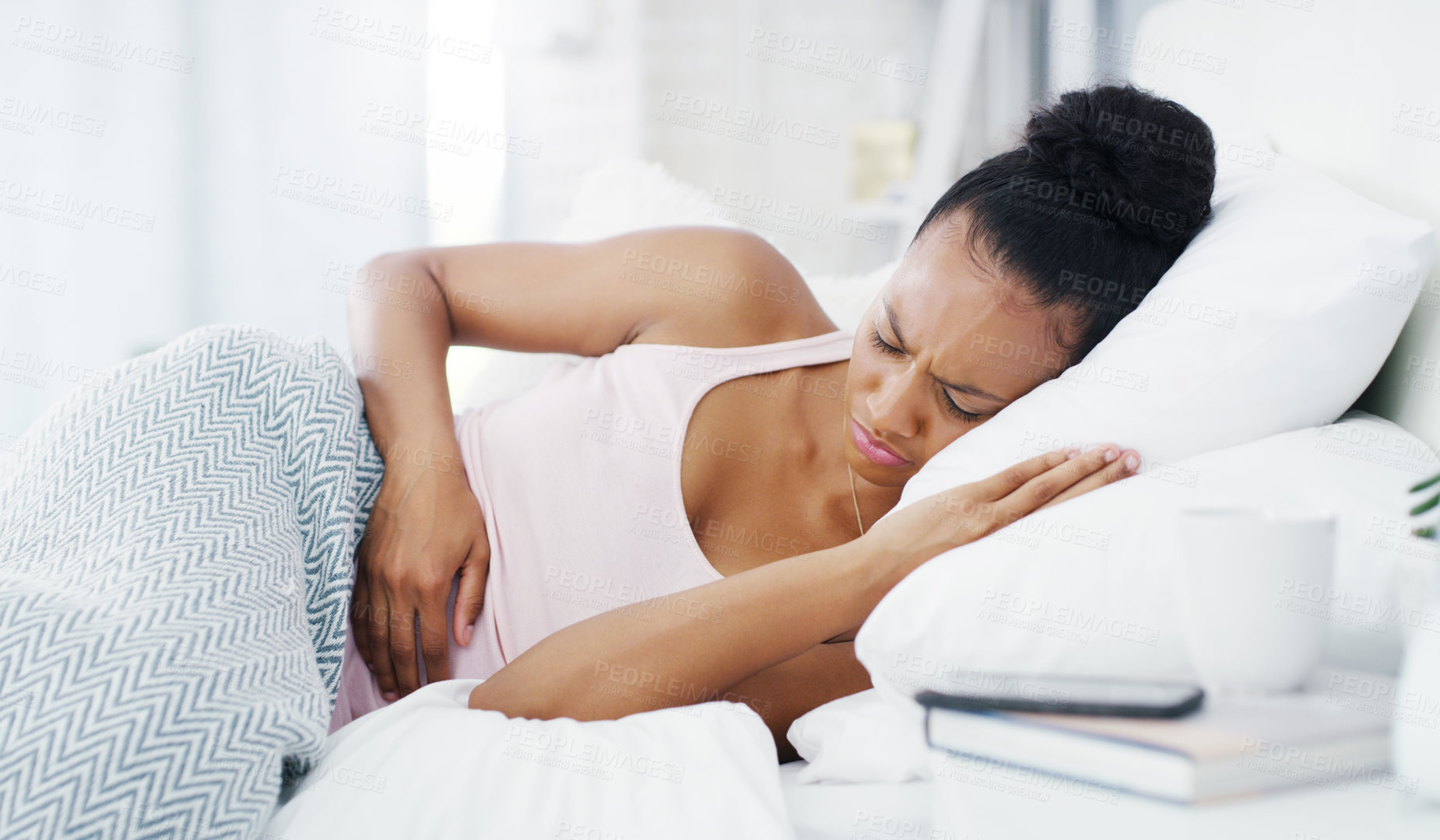 Buy stock photo Shot of an attractive young woman suffering from stomach cramps while lying in her bed at home