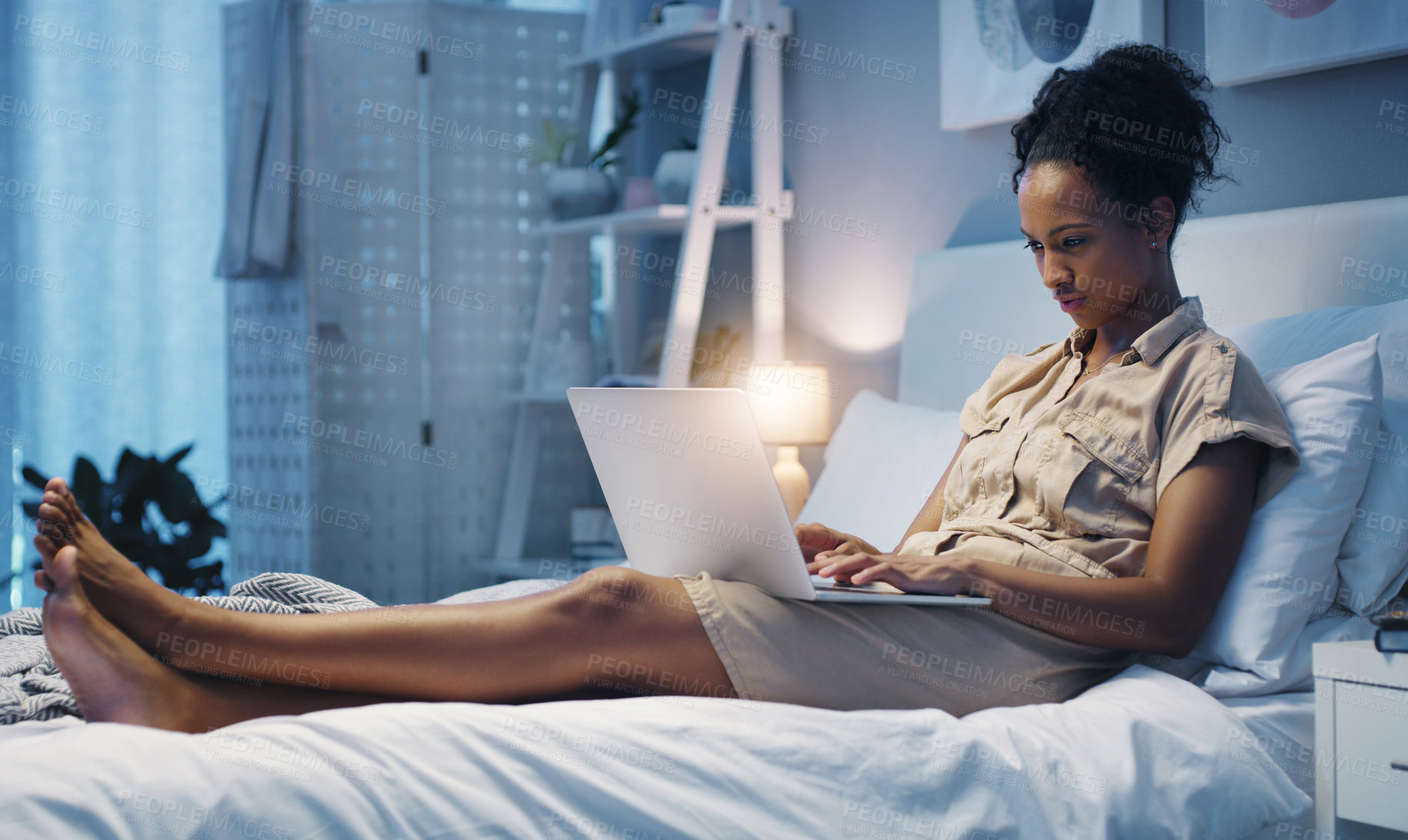 Buy stock photo Shot of an attractive young woman using her laptop while lying on her bed after a long day at work