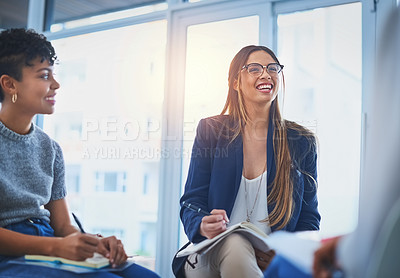 Buy stock photo Shot of two attractive young businesswomen taking down notes on their notepad's during a meeting at work