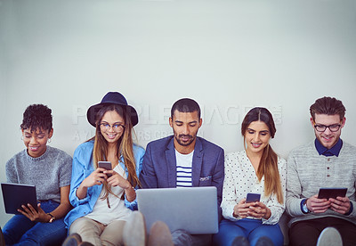 Buy stock photo Studio shot of a group of young businesspeople using wireless technology while sitting in line against a grey background