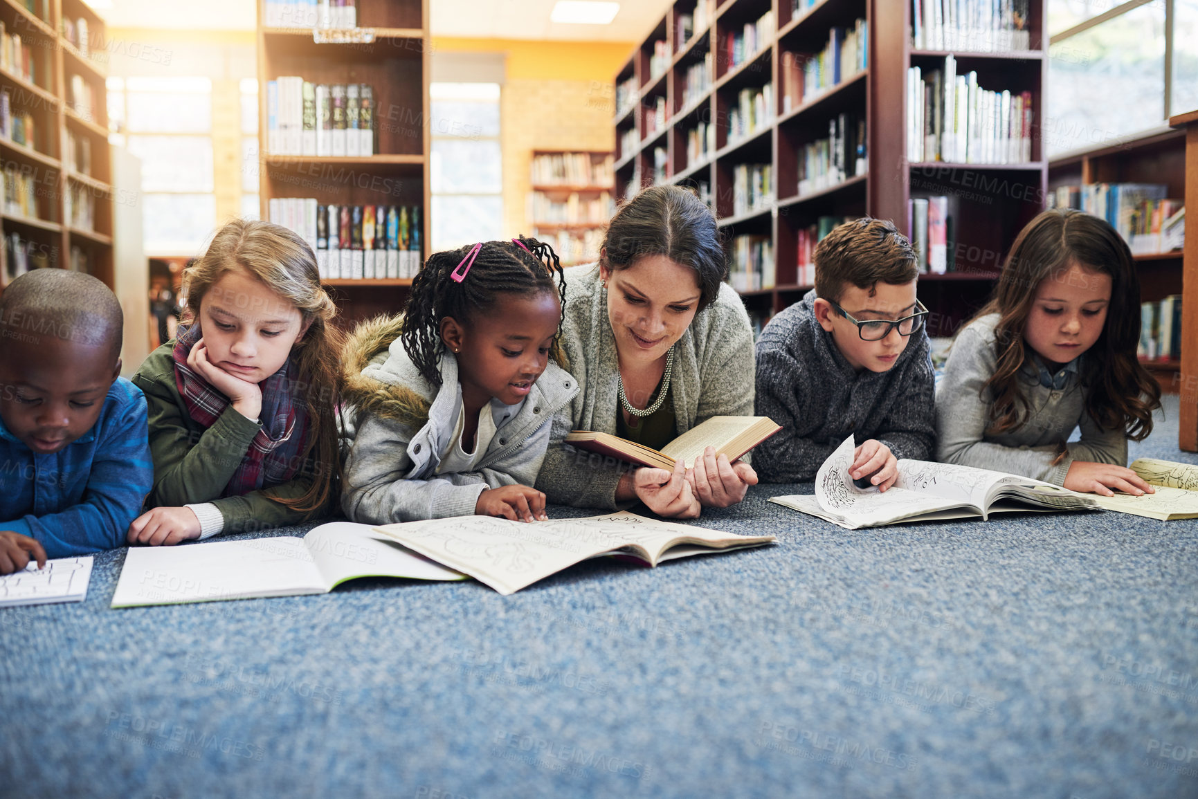 Buy stock photo Teacher, children and books on floor, lying and reading at library, education and studying for future. Woman, kids and relax on carpet with learning, development and scholarship in hall at school