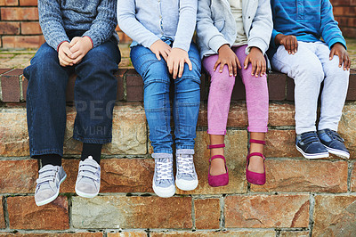 Buy stock photo Shot of a group of unrecognizable elementary school kids sitting on a brick wall outside