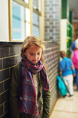 Buy stock photo Shot of an elementary school girl leaning against a wall while standing in the corridor at school