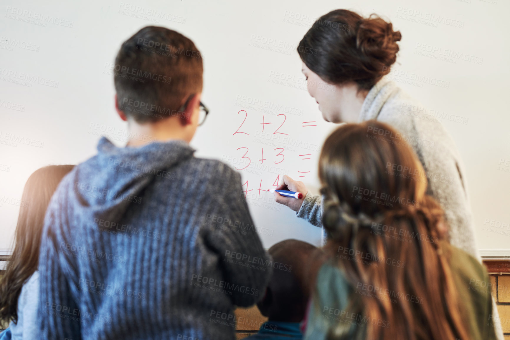 Buy stock photo Rearview shot of teacher and her students doing math equations on a white board in class