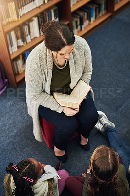 Buy stock photo High angle shot of a teacher reading to a group of elementary school kids in the library