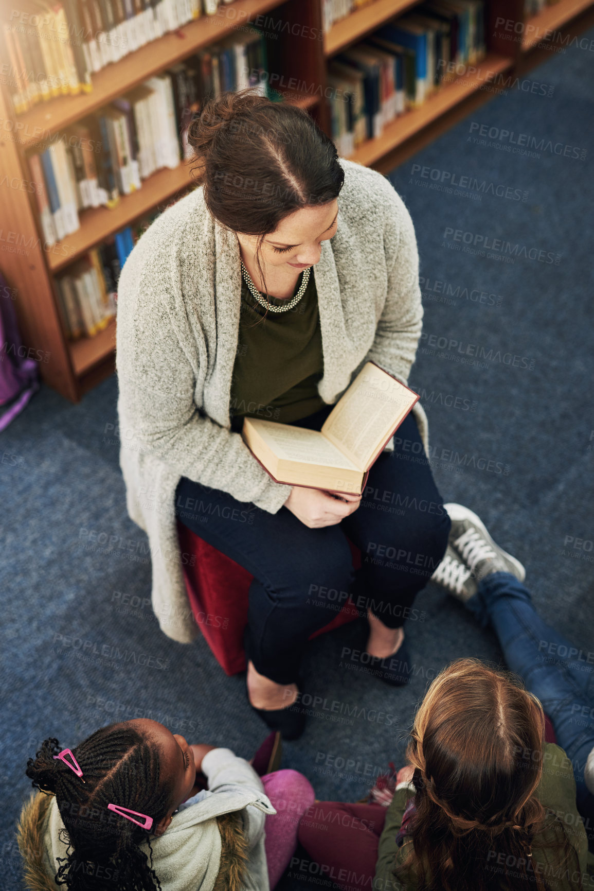 Buy stock photo High angle shot of a teacher reading to a group of elementary school kids in the library