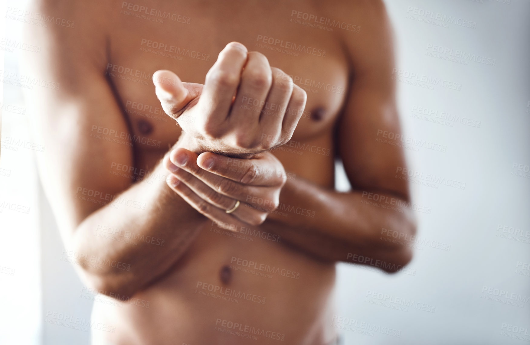 Buy stock photo Shot of a shirtless unrecognizable man holding his wrist in discomfort due to pain inside at home