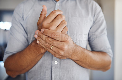 Buy stock photo Shot of an unrecognizable man holding his wrist in pain while relaxing at home
