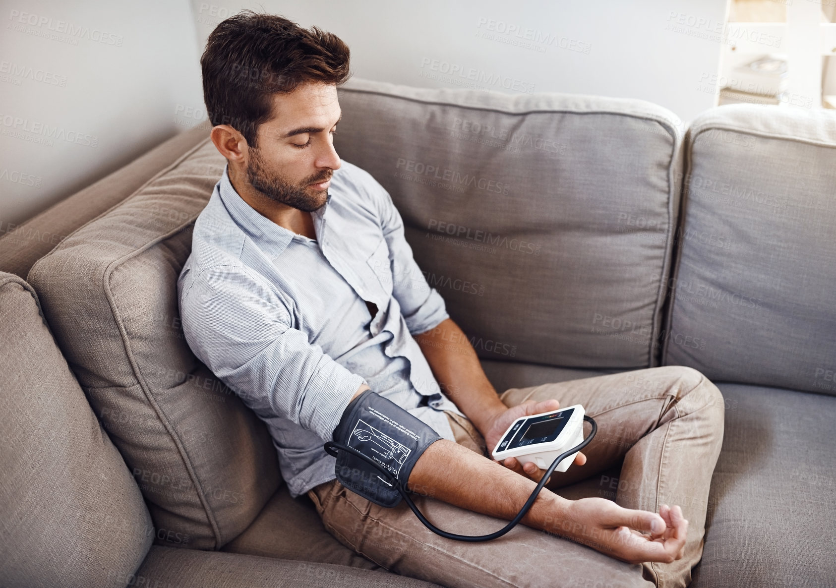 Buy stock photo Shot of a young man taking his own blood pressure readings with a blood pressure monitor at home