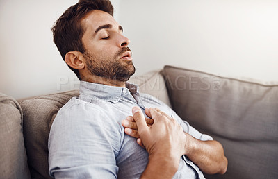 Buy stock photo Shot of a handsome young businessman holding his chest in pain while relaxing on a sofa at home
