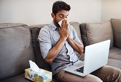 Buy stock photo Shot of a young businessman blowing his nose with a tissue while trying to work on his laptop at home