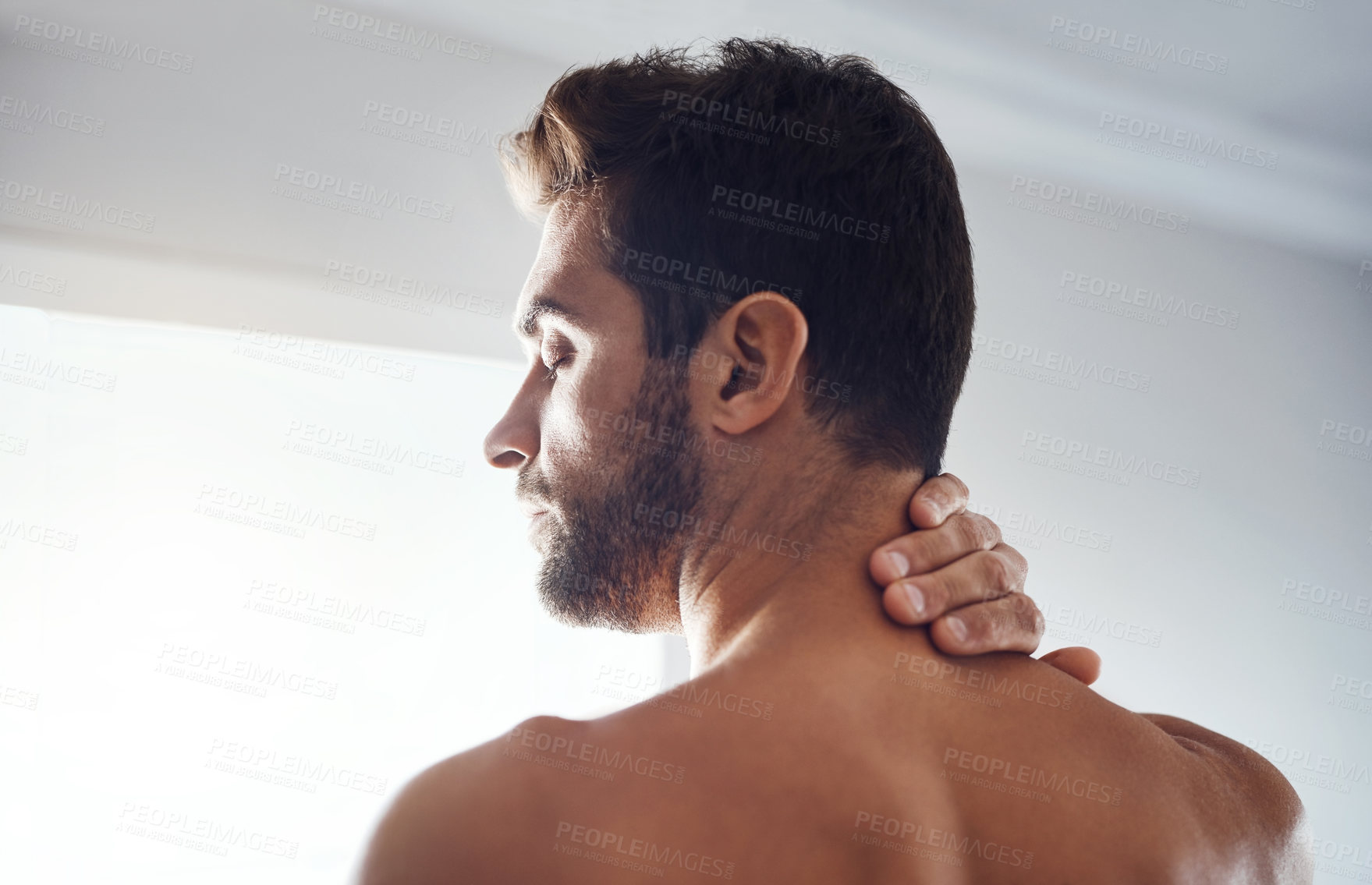 Buy stock photo Rearview shot of a handsome young man holding his neck in pain while relaxing at home