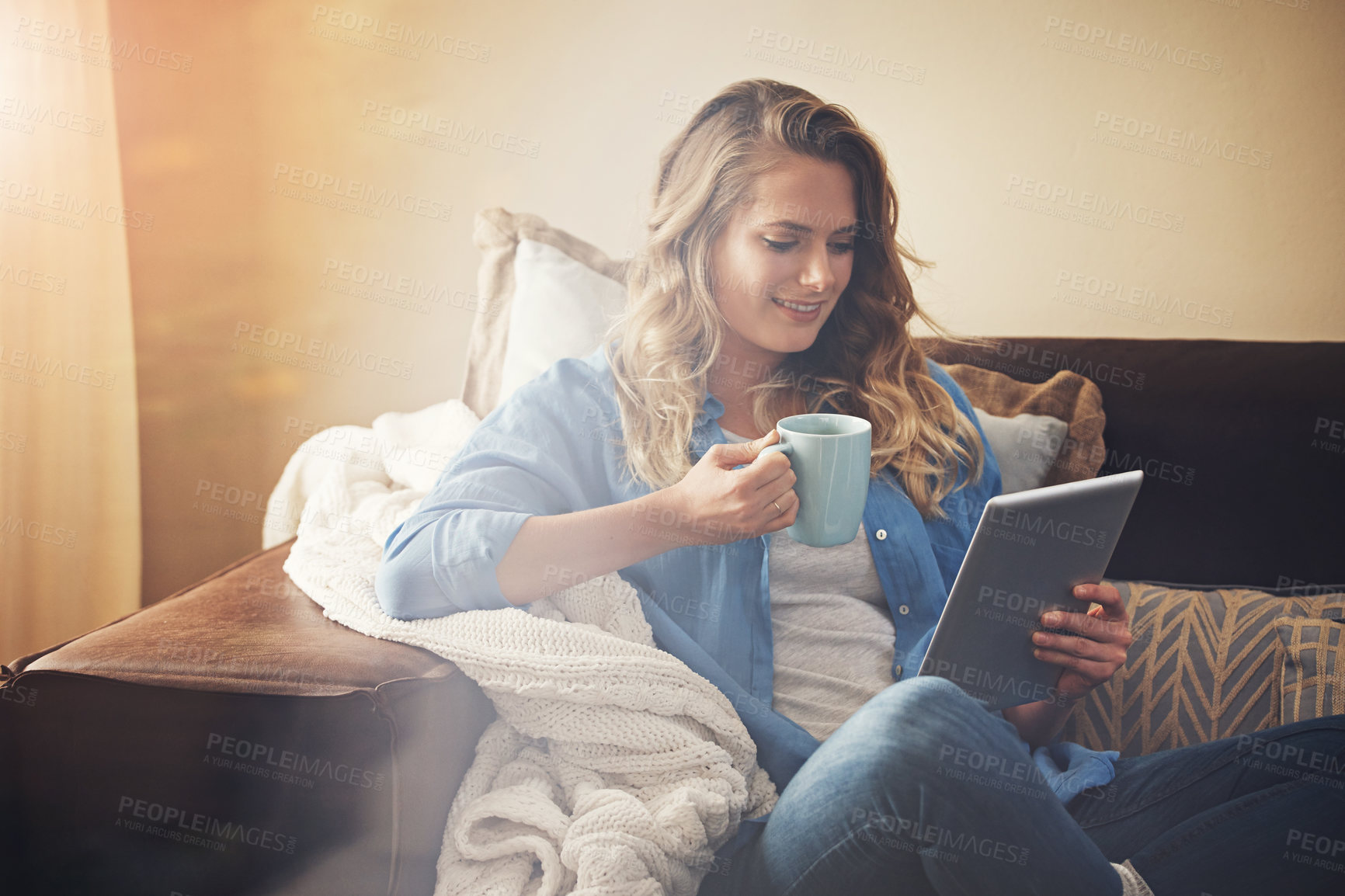 Buy stock photo Shot of a relaxed young woman having coffee and using a digital tablet on the sofa at home